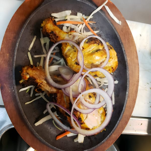 Grand India's sizzling tandoori chicken drumsticks with onion and cabbage on a cast iron platter.