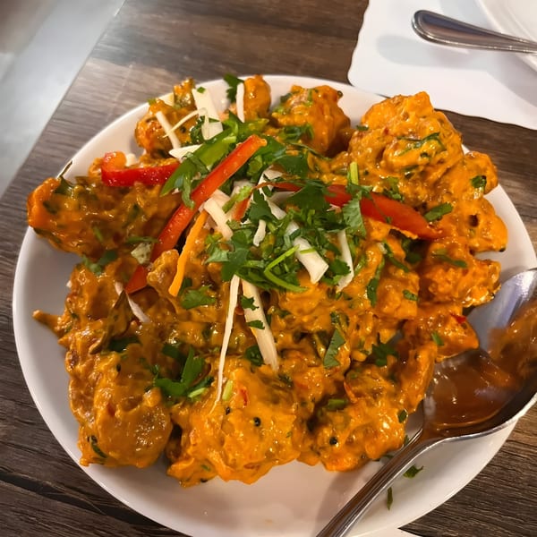 Grand India's vibrant orange Indian dish, garnished with fresh cilantro, red peppers, and white strips.
