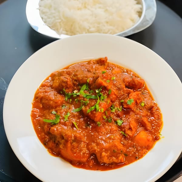 Grand India's chicken curry with cilantro on a white plate, with a side of white rice.