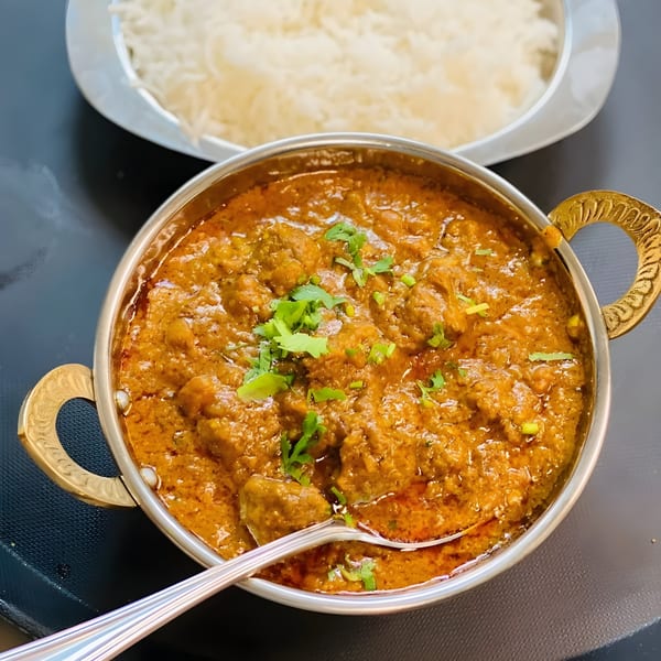 Grand India's rich Indian curry in a metal bowl with a spoon, served with white rice.