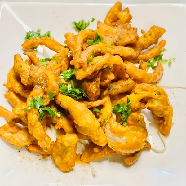 Grand India's crispy onion bhaji, golden-brown and garnished with fresh green cilantro on a white plate.