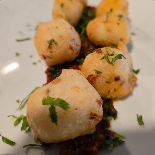 Golden-fried Indian fritters, garnished with fresh herbs, served on a rich, dark sauce.