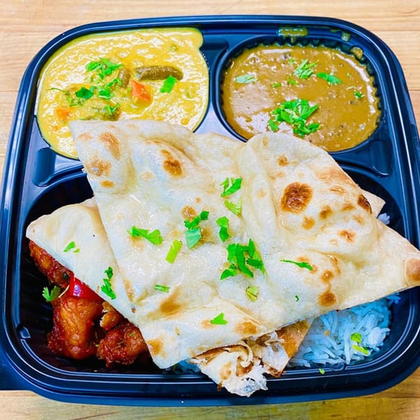 Grand India's Indian takeout meal with naan, rice, chicken, and two curries in a black container.